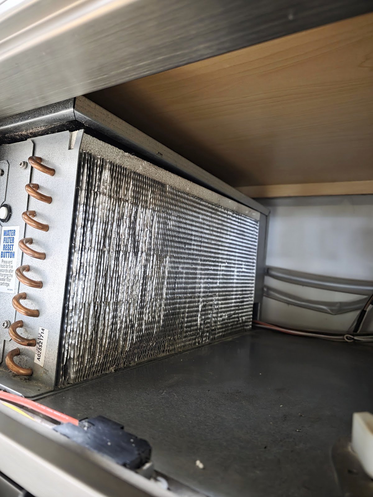 Condenser coil behind the upper grille of a built-in refrigerator
