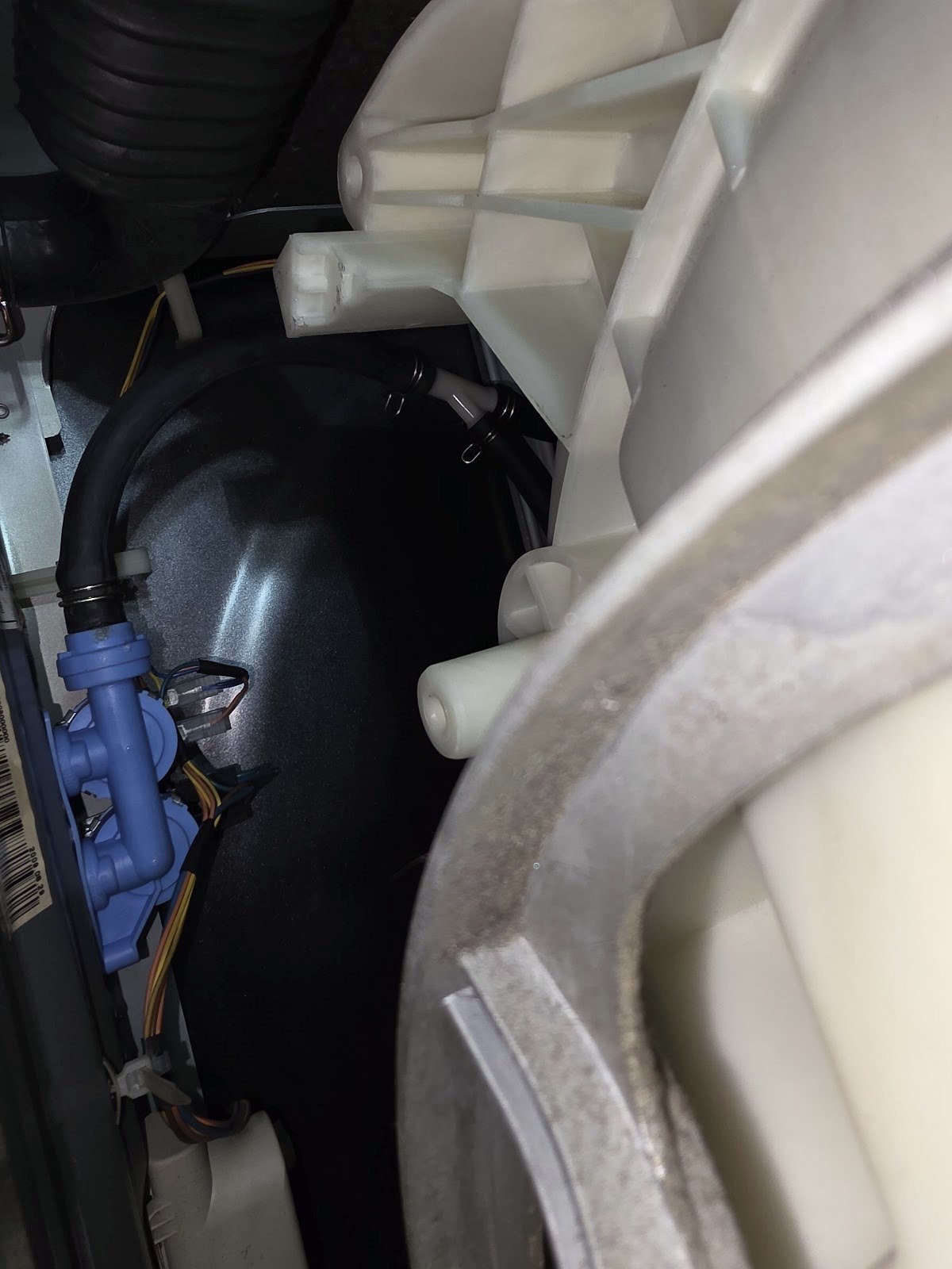 Close-up of a dishwasher pump and hose connections beneath the tub
