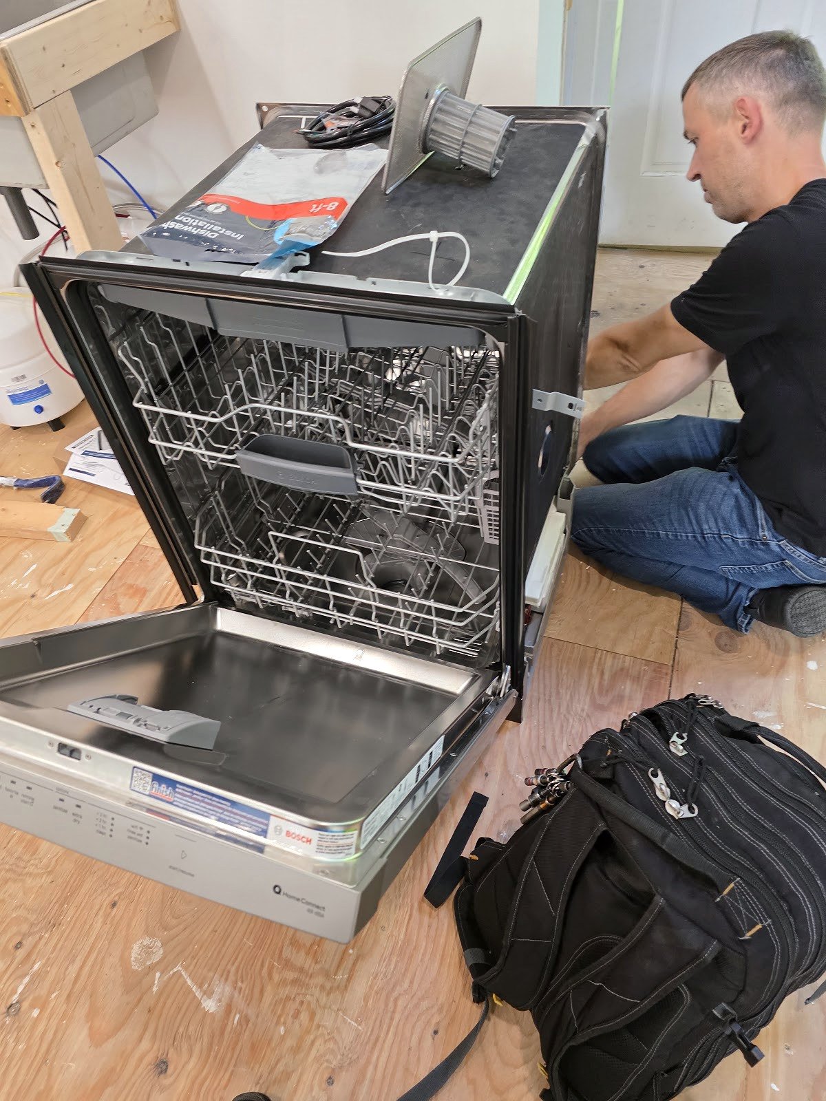 Technician working beside an opened dishwasher with tools nearby