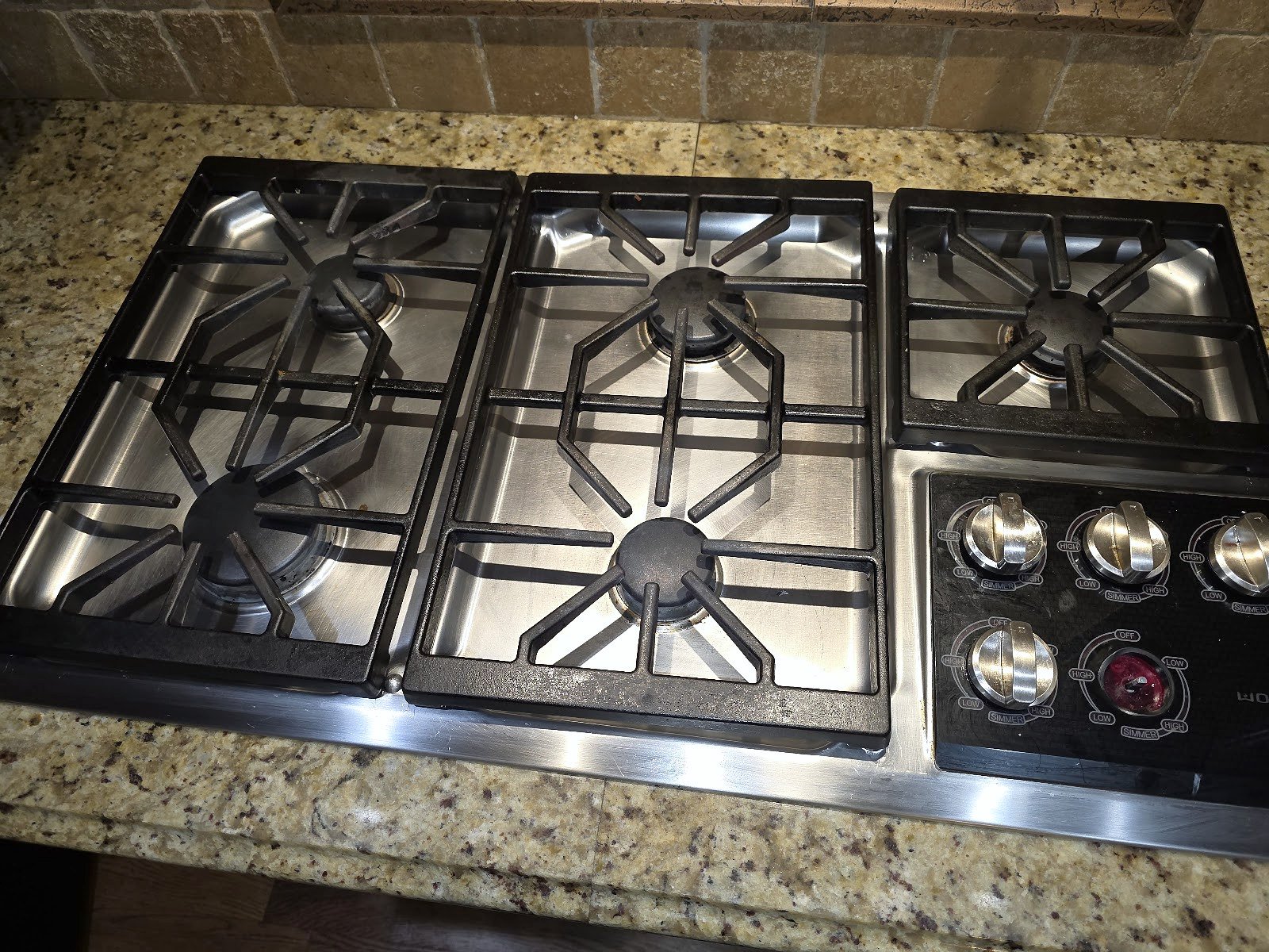 Black gas cooktop with grates and burner caps in a kitchen counter