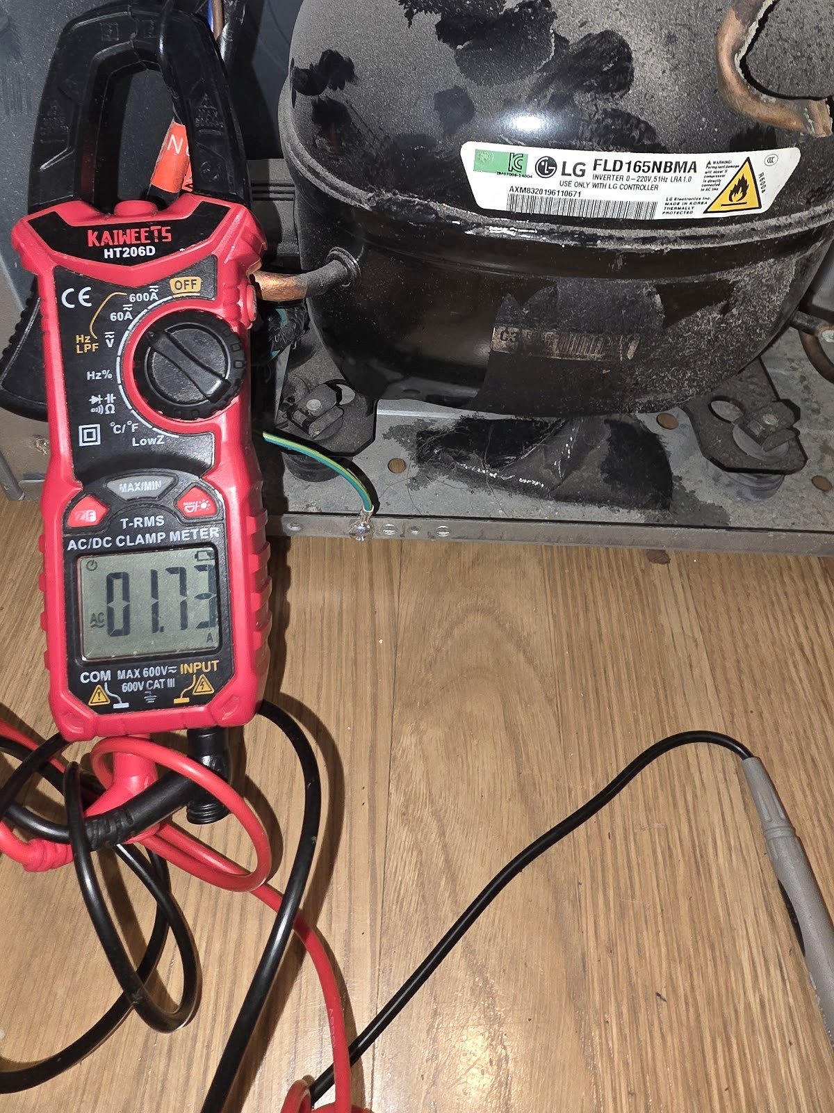 Clamp meter and leads beside a refrigerator compressor