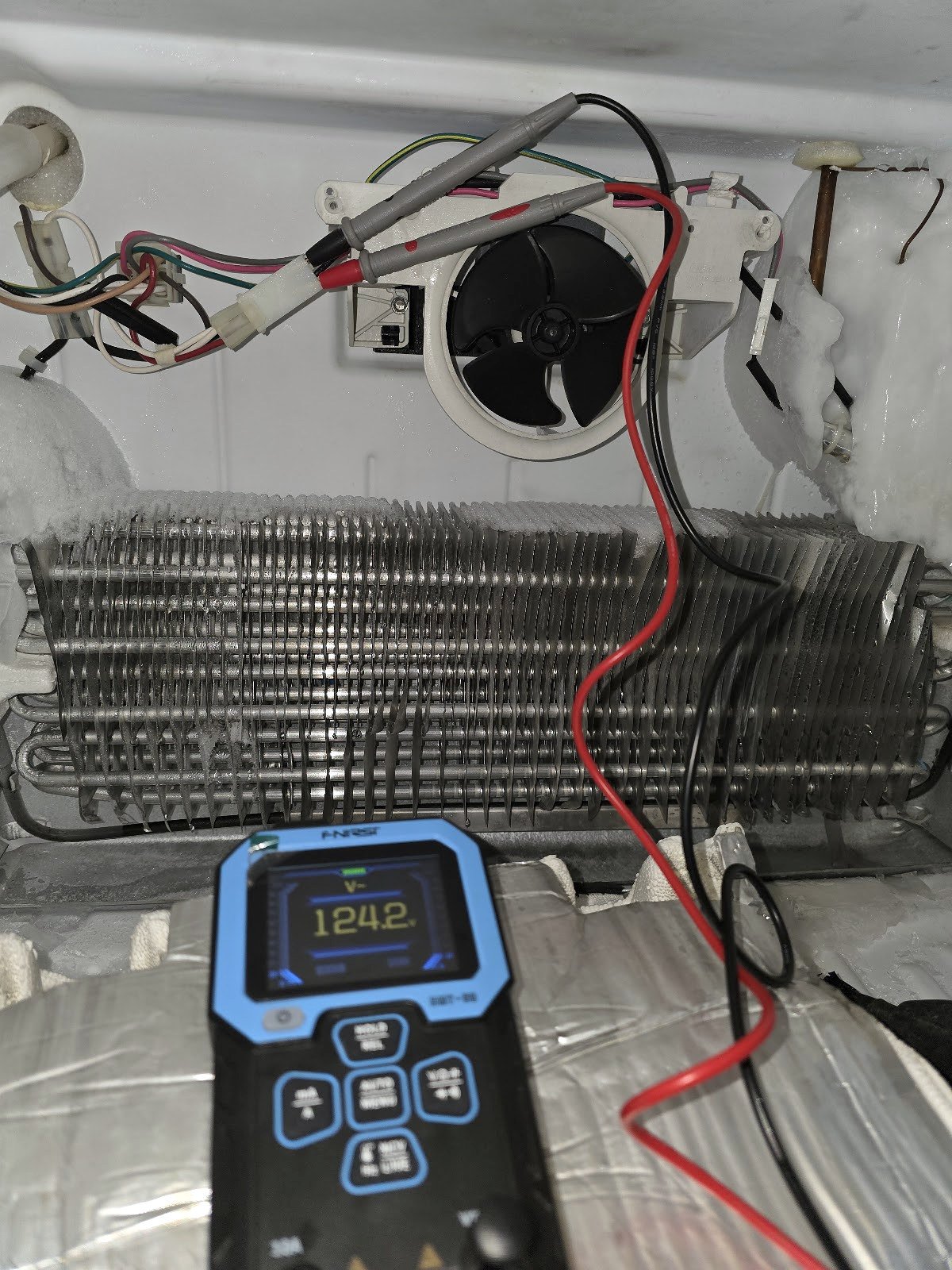 Meter and test leads beside an exposed refrigerator evaporator and fan
