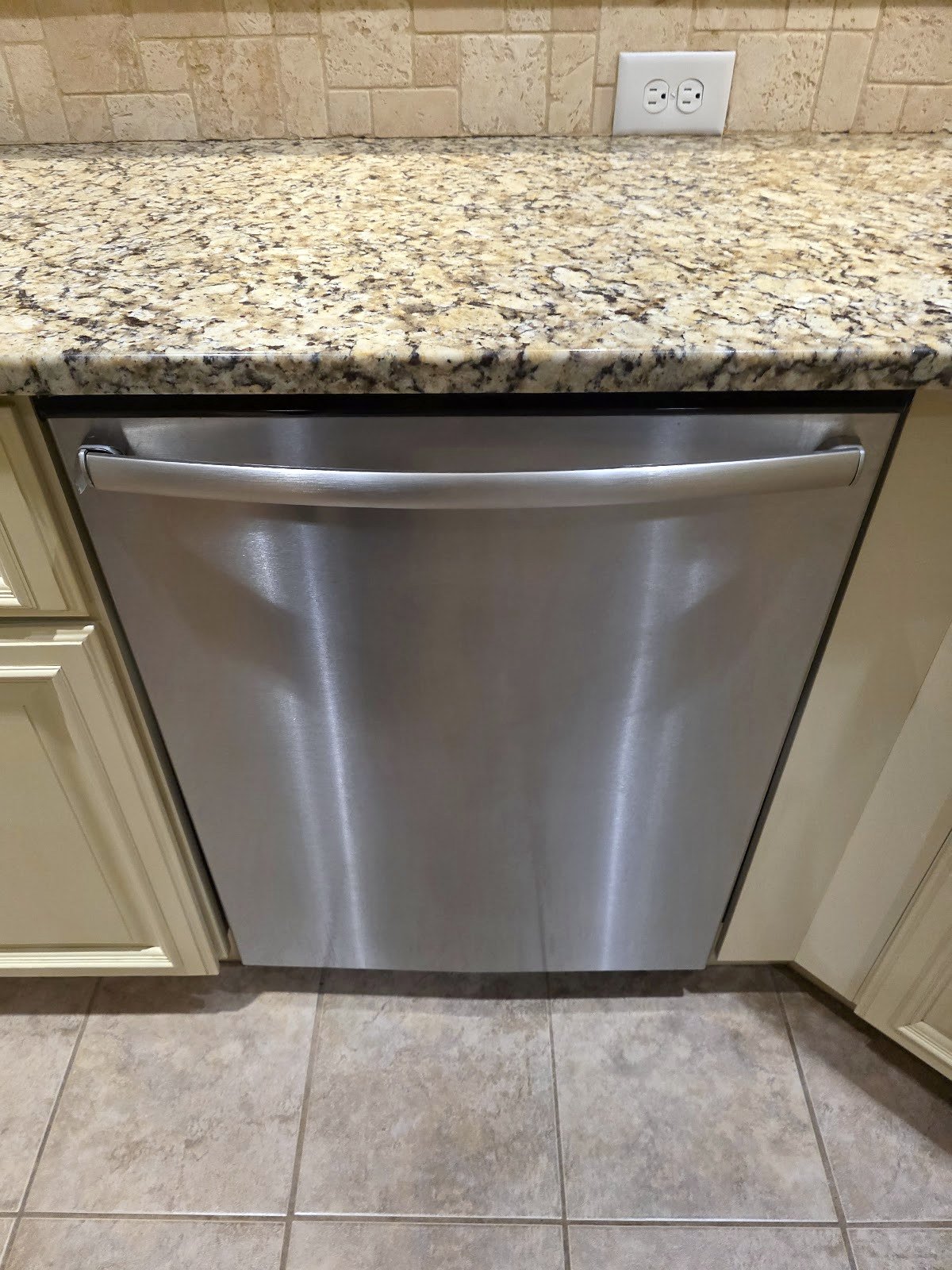 Stainless steel dishwasher beneath a light stone countertop