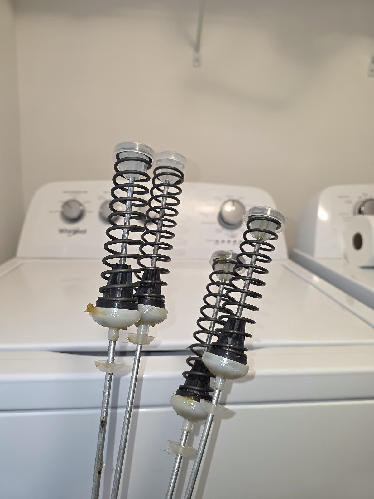Washer suspension rods and springs laid out beside a top-load washer