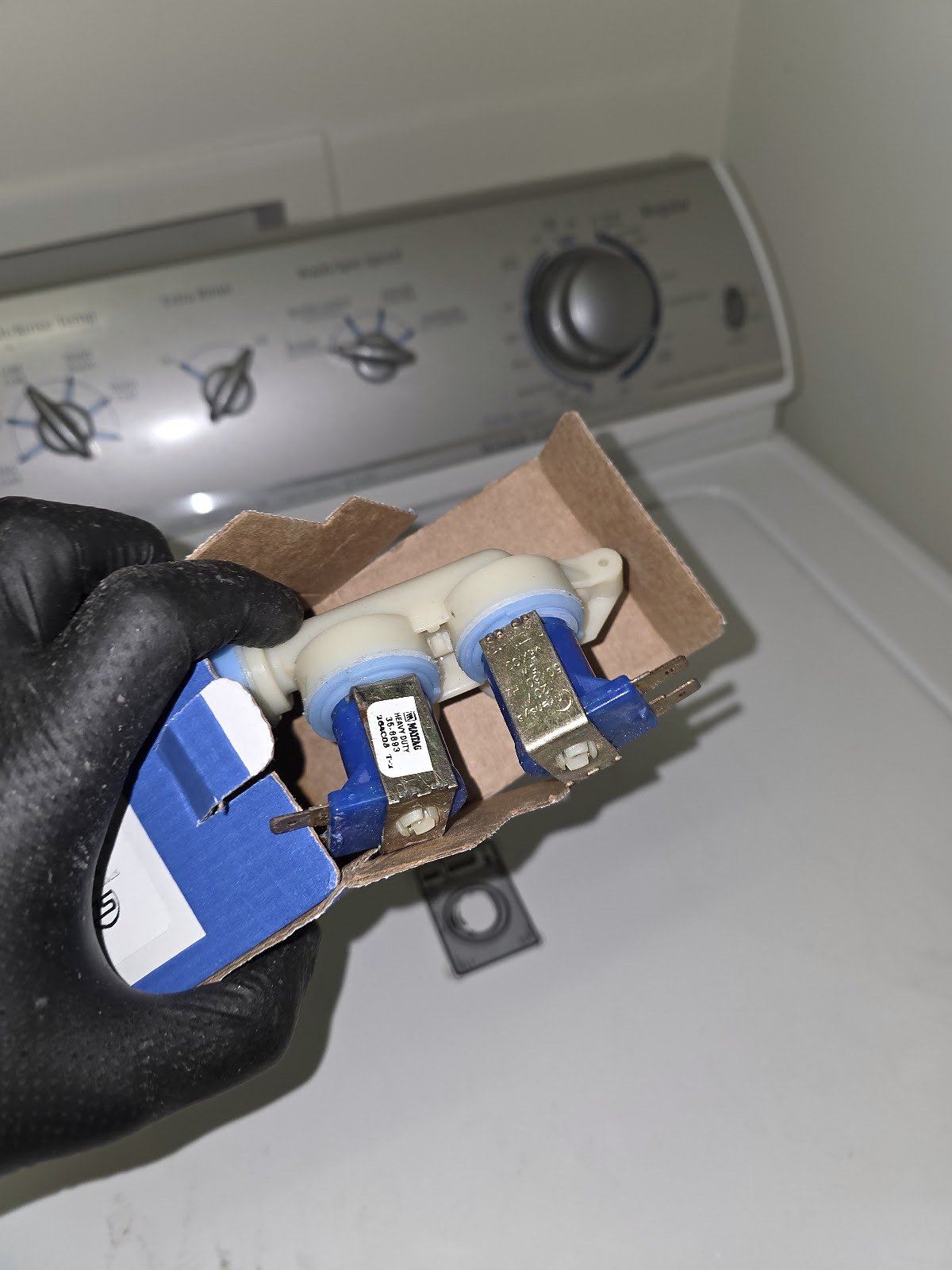 Technician holding a washing machine water inlet valve beside a top-load washer